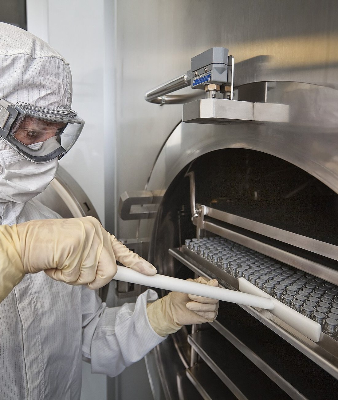 A gowned operator loading a tray of crimp-sealed vials into a freeze dryer